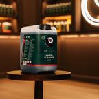 A large plastic jug of Better Wheel Cleaner sits on a round wooden stool in a warmly lit indoor setting with blurred shelves and lighting in the background.