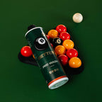 A bottle of Better Pool Pre-Wash liquid lies on a green pool table next to a rack of colorful billiard balls, with one white ball in the background.