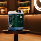 A large plastic canister of Better Brand Rinse Aid sits on a small round wooden table in a warmly lit, blurred indoor setting with shelves in the background.