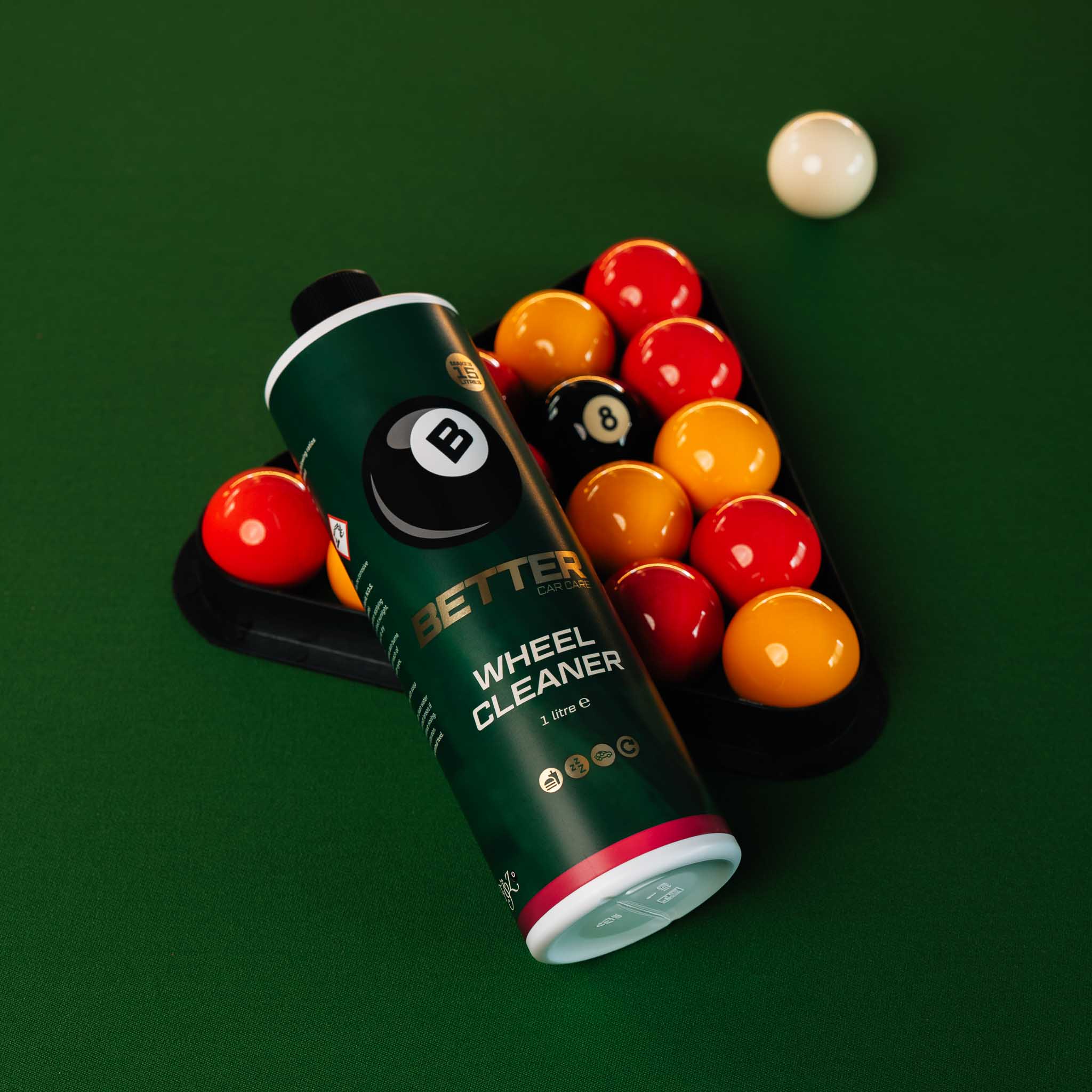 A tube of Better 8 Wheel Cleaner lies on a green pool table next to a rack of billiard balls, with a white cue ball in the upper right.